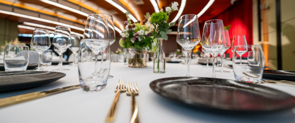 Festlich gedeckter Bankett-Tisch mit Weingläsern, goldenem Besteck und Blumendekoration bei stimmungsvoller Beleuchtung – Eventausstattung von Partyladen von Voss