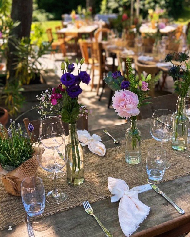 Gedeckter Gartentisch mit bunten Blumenvasen, Weingläsern und Stoffservietten – Beispiel für Outdoor-Eventdeko von Partyladen von Voss